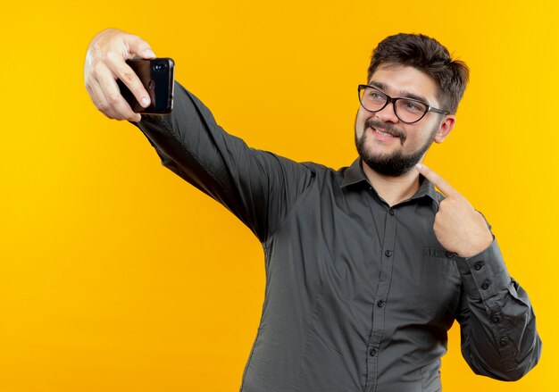 Ein zufriedener junger Geschäftsmann mit Brille macht ein Selfie und zeigt auf sich