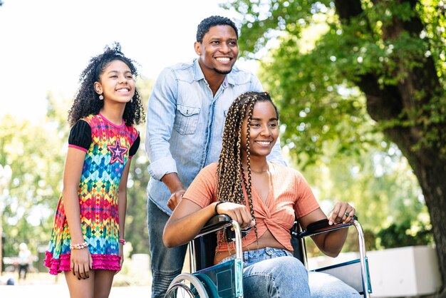 Eine Afroamerikanerin im Rollstuhl, die mit ihrer Tochter und ihrem Ehemann einen Spaziergang im Freien genießt.