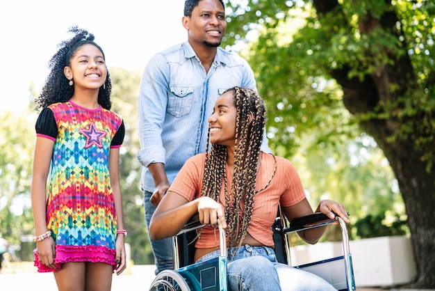 Eine Afroamerikanerin im Rollstuhl, die mit ihrer Tochter und ihrem Ehemann einen Spaziergang im Freien genießt.