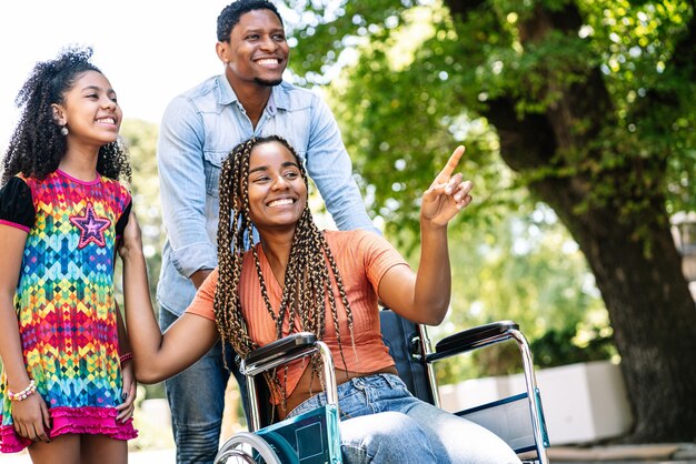 Eine Afroamerikanerin im Rollstuhl, die mit ihrer Tochter und ihrem Ehemann einen Spaziergang im Freien genießt.