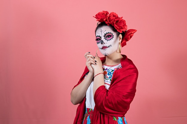 Eine als catrina verkleidete junge frau in mexikanischem kostüm, die vor einem schlichten hintergrund posiert