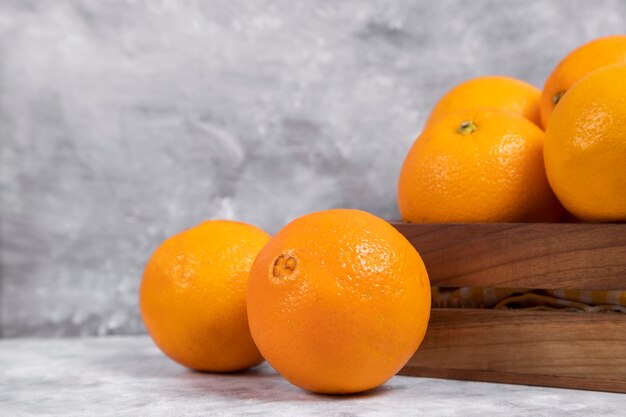 Eine alte Holzkiste voller ganzer und geschnittener Orangenfrüchte auf Marmor