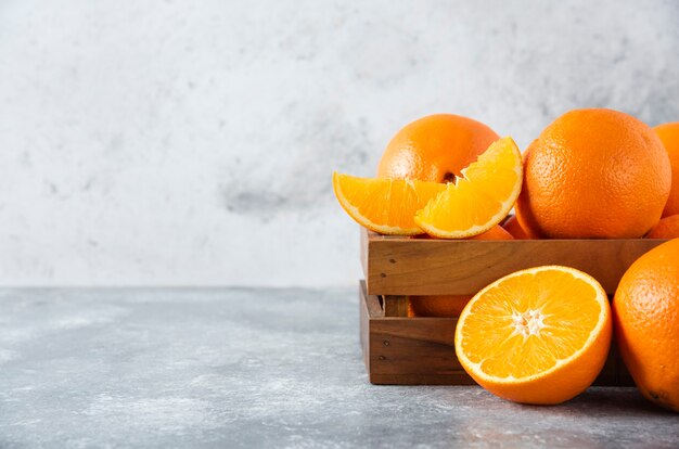 Eine alte Holzkiste voller saftiger Orangenfrüchte auf Steintisch.