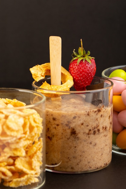 Eine Ansicht des braunen Schoko-Desserts der Vorderansicht leckeres leckeres süßes mit Schokoladenpulver-Schokoriegel und Erdbeere mit Cornflakes und Bonbons auf dem dunklen Hintergrund süßes Erfrischungsdessert