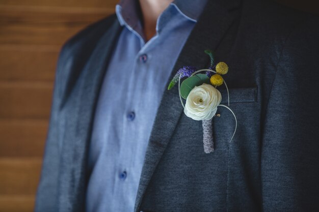 Eine Anstecknadel aus Rosenweißrose und gelben Blüten in der Jacke eines Mannes.