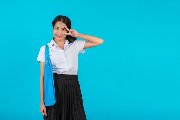 Eine asiatische Studentin, die eine Stofftasche spinnt und verschiedene Gesten auf einem Blau zeigt.