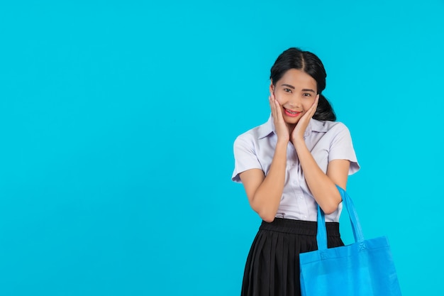 Eine asiatische Studentin, die eine Stofftasche spinnt und verschiedene Gesten auf einem Blau zeigt.