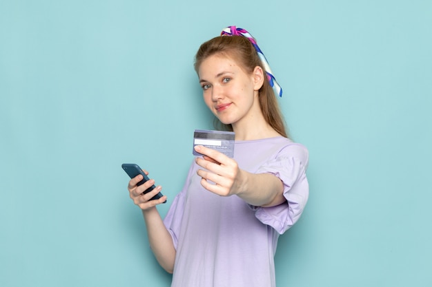 Eine attraktive Frau der Vorderansicht im blauen Hemdkleid, das ein auf Blau lächelndes Telefon hält und verwendet