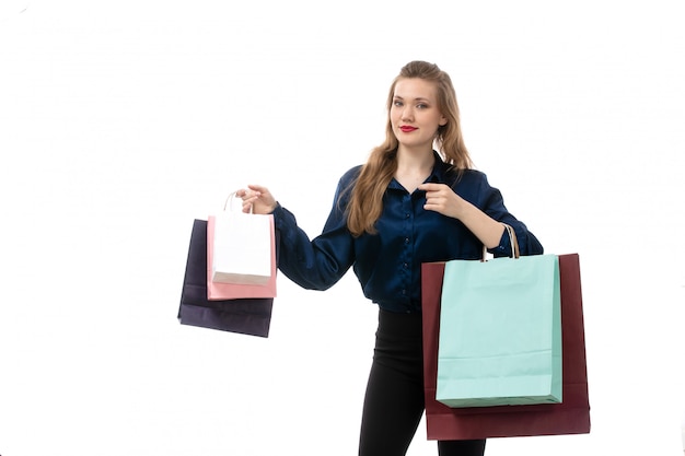 Eine attraktive junge Dame der Vorderansicht in der schwarzen Hose der blauen Bluse, die Einkaufspakete auf der eleganten Kleidung des weißen Hintergrundmode aufwirft