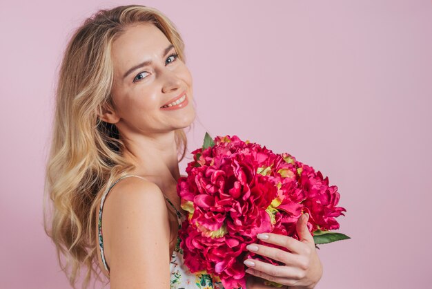 Eine attraktive junge Frau, die schöne rote Blumen gegen rosa Hintergrund hält