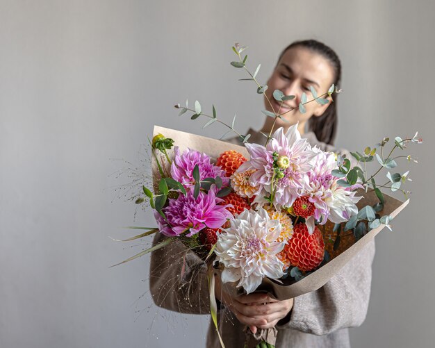 Eine attraktive junge Frau lächelt und hält einen großen festlichen Blumenstrauß mit Chrysanthemen und anderen Blumen in ihren Händen.