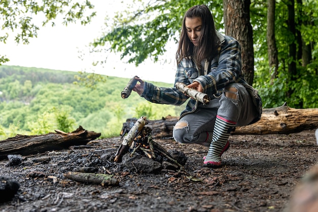 Eine attraktive junge Frau macht ein Feuer, um sich im Wald warm zu halten.