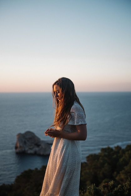 Eine attraktive junge Frau mit einem schönen weißen Kleid, das am Abend am Meer spazieren geht