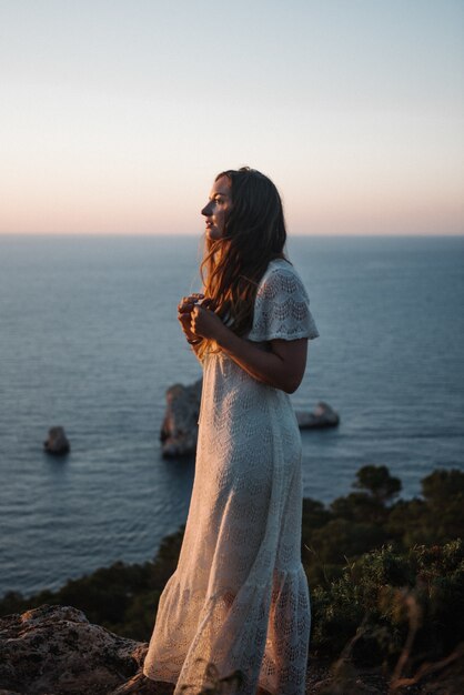 Eine attraktive junge Frau mit einem schönen weißen Kleid, das am Abend am Meer spazieren geht