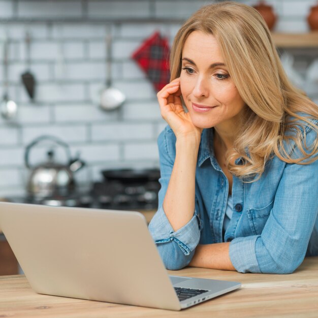 Eine attraktive junge Geschäftsfrau, die Laptop auf Holztisch betrachtet