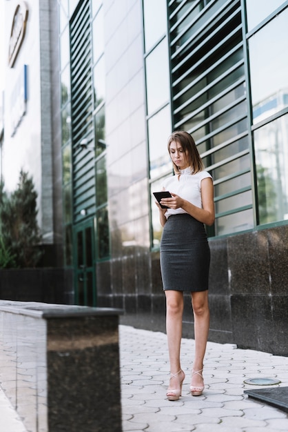 Eine attraktive junge Geschäftsfrau, die Smartphone an draußen verwendet