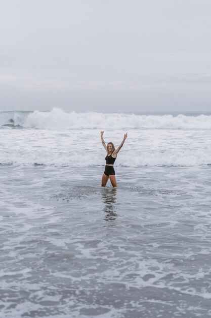 Eine barfüßige junge Frau mit einem schlanken Körper läuft auf der Meeresbrandung am Wasserbecken, um sich fit zu halten und Fett zu verbrennen. Strandhintergrund mit blauem Himmel. Frauenfitness, Joggen, sportliche Aktivitäten auf einer Sommerfami