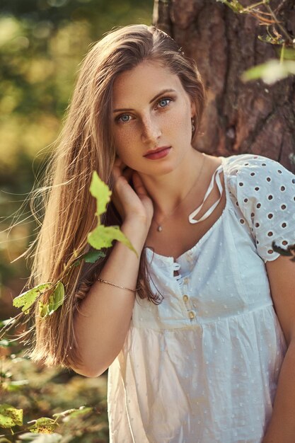 Eine bezaubernde schöne Frau in einem weißen Kleid, das in einem grünen Herbstwald aufwirft.