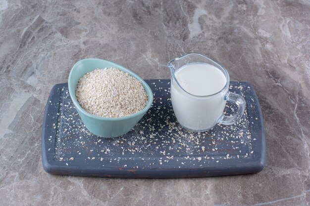 Eine blaue Schüssel Reis mit einer Glastasse Milch auf einem Holzbrett