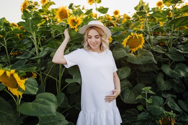 Eine blonde Frau in einem weißen Kleid auf dem Feld mit Sonnenblumen