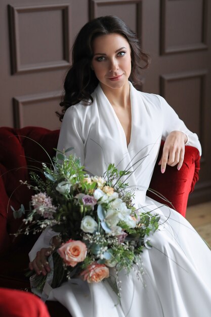 Eine Braut im Hochzeitskleid sitzt auf der roten Bank mit einem Blumenstrauß