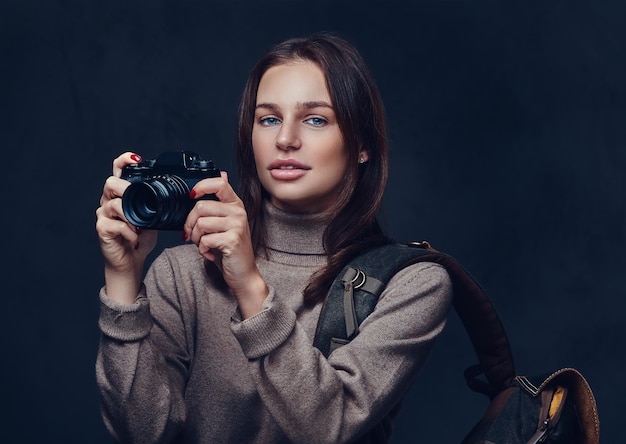 Eine brünette Reisende mit Rucksack hält eine kompakte Fotokamera.