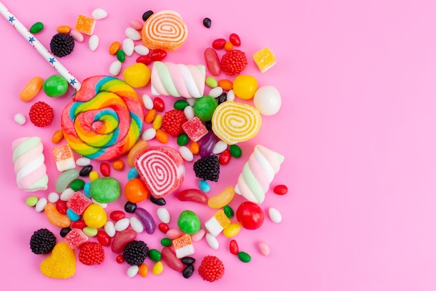 Eine bunte Bonbonzusammensetzung der Draufsicht von verschiedenfarbigen süßen und köstlichen Bonbons auf rosa Schreibtisch