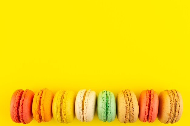 Eine bunte französische Macarons der Draufsicht, die auf dem gelben Schreibtischzuckerkuchenkeks süß schmeckt