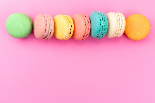 Eine bunte köstliche runde köstliche französische Macarons der Draufsicht, die auf rosa Kuchen-Keks-Süßwaren ausgekleidet ist