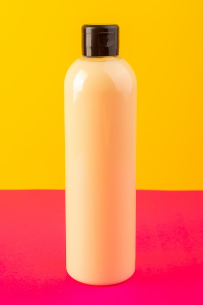 Eine cremefarbene Flasche Plastikshampoo-Dose der Vorderansicht mit schwarzer Kappe lokalisiert auf dem rosa-gelben Hintergrundkosmetik-Schönheitshaar