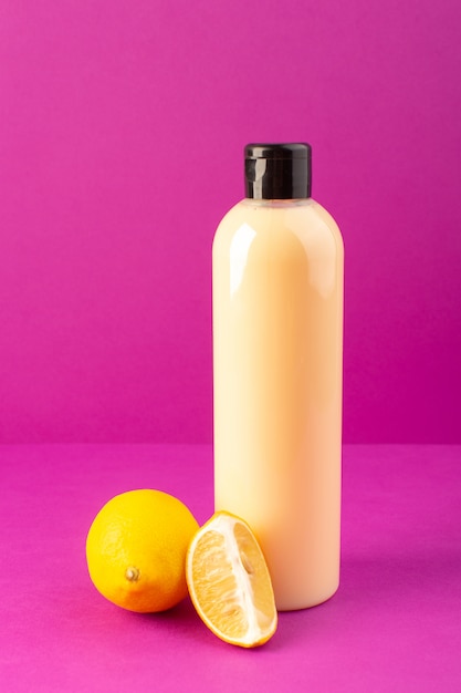 Eine cremefarbene Flasche Plastikshampoo-Dose der Vorderansicht mit schwarzer Kappe zusammen mit Zitronen, die auf dem Schönheitshaar der purpurnen Hintergrundkosmetik isoliert werden