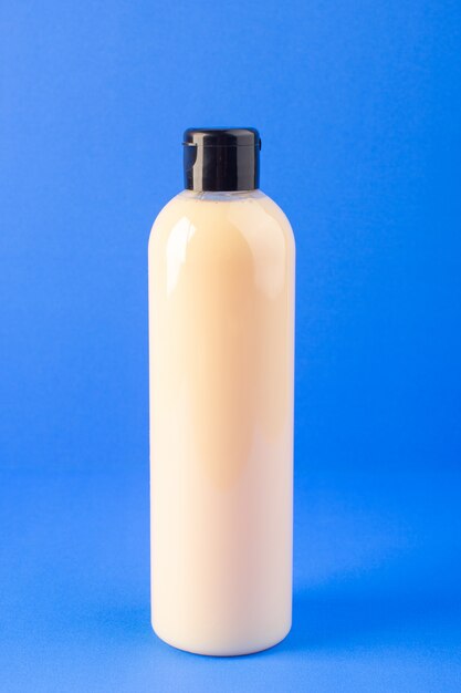 Eine cremefarbene Plastik-Shampoo-Dose der Vorderansicht mit schwarzer Kappe, die auf dem Schönheitshaar der blauen Hintergrundkosmetik isoliert wird