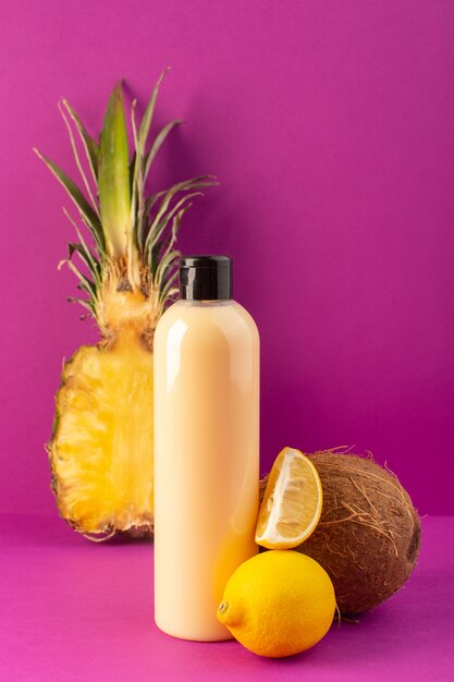 Eine cremefarbene Plastik-Shampoo-Dose der Vorderansicht mit schwarzer Kappe zusammen mit Zitronenananas und Kokosnuss, die auf den Schönheitsfrüchten des lila Hintergrundkosmetiks isoliert werden