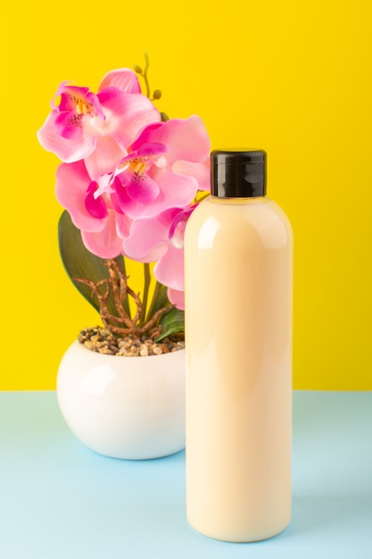 Eine cremefarbene Plastik-Shampoo-Dose mit Vorderansicht und schwarzer Kappe, die zusammen mit Blumen auf dem gelb-eisblauen Hintergrundkosmetik-Schönheitshaar isoliert ist