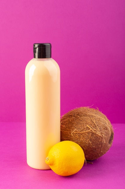 Eine cremefarbene Plastik-Shampoo-Dose mit Vorderansicht und schwarzer Kappe zusammen mit Zitronen und Kokosnuss, die auf dem Schönheitshaar der lila Hintergrundkosmetik isoliert sind