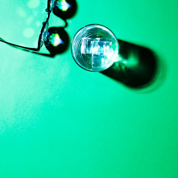 Eine Draufsicht auf Brillen und Wasserglas mit Schatten auf grünem Hintergrund