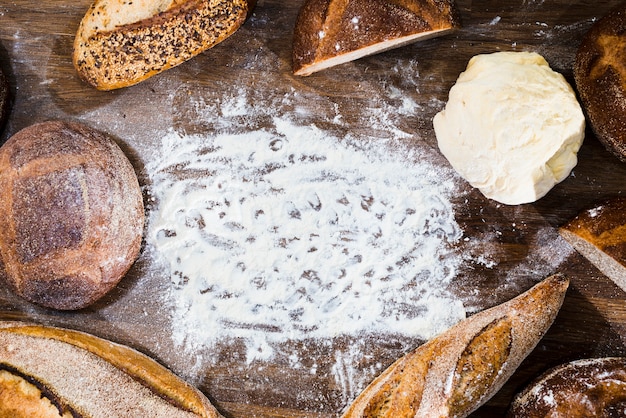 Eine Draufsicht auf Brot; Stangenbrot und gekneteter Teig mit Mehl auf hölzernem Schreibtisch