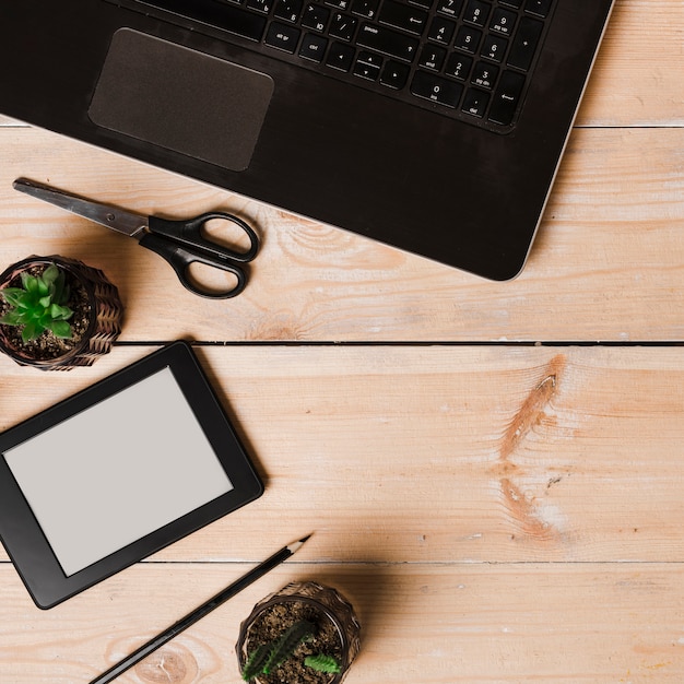 Kostenloses Foto eine draufsicht auf eine topfpflanze; bleistift; schere; laptop- und ebookleser auf holztisch