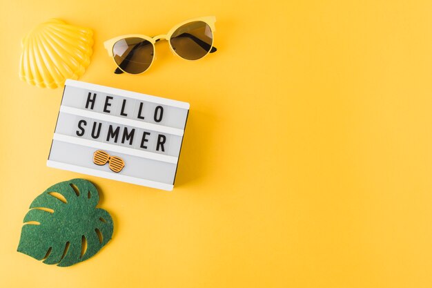 Eine Draufsicht auf Jakobsmuschel; Sonnenbrille; Blatt und hallo Sommerlichtkasten auf gelbem Hintergrund