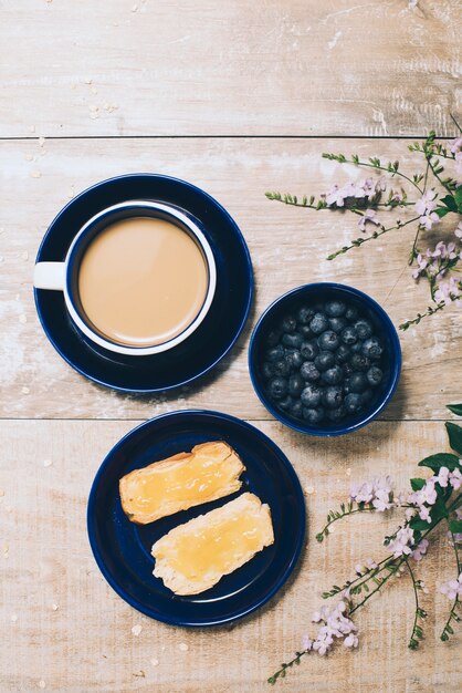 Eine Draufsicht auf Kaffee; Blaubeeren; Toast und Blumen auf Schreibtisch aus Holz