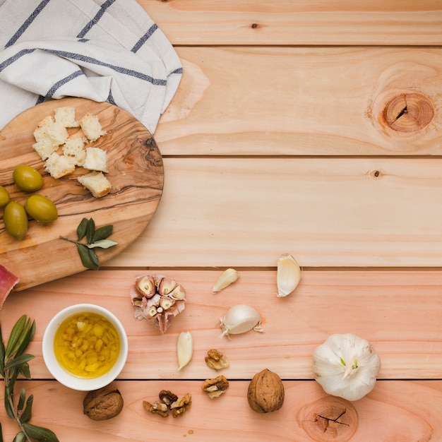Eine Draufsicht auf Oliven; Brot; Walnüsse und hineingegossene Olivenöle auf Holztisch