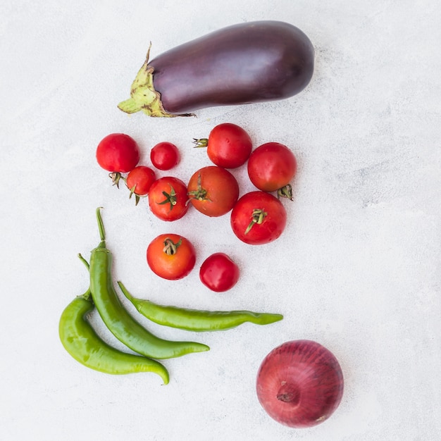 Kostenloses Foto eine draufsicht auf tomaten; grüne chilis; zwiebel und aubergine auf weißem strukturiertem hintergrund