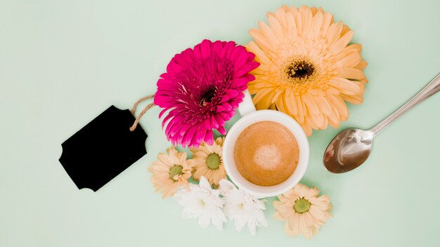 Eine Draufsicht der Kaffeetasse mit Blumendekoration und schwarzem leerem Tag auf farbigem Hintergrund