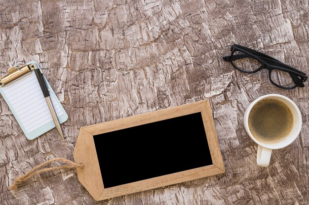 Eine Draufsicht der Kaffeetasse; Stift; kleine Zwischenablage und Brillen auf strukturierten Hintergrund