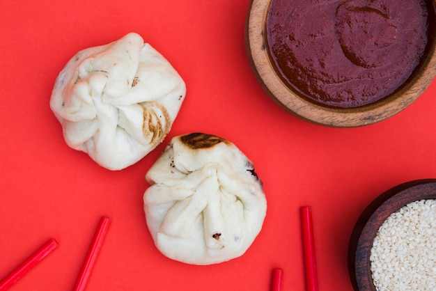 Kostenloses Foto eine draufsicht der knödel; essstäbchen; sesam und saucen auf rotem hintergrund