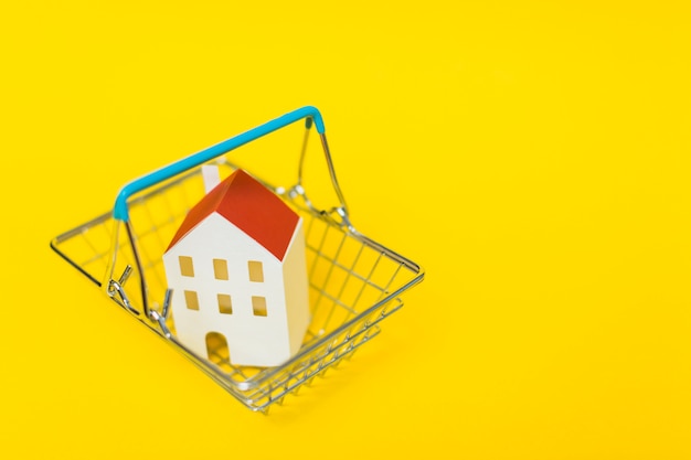 Eine Draufsicht des Hausmodells innerhalb des Einkaufswagens gegen gelben Hintergrund