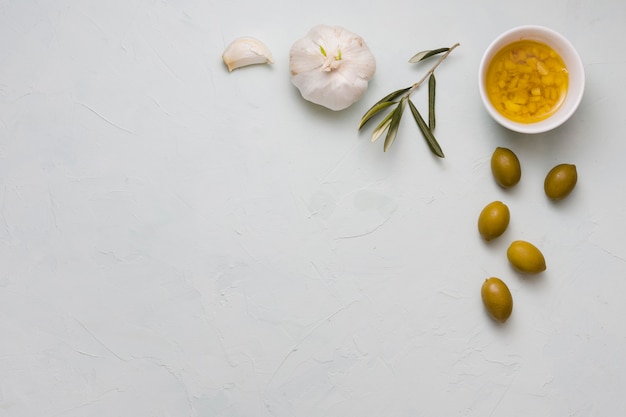 Eine Draufsicht des hineingegossenen Olivenöls und des Knoblauchs in der Schüssel auf konkretem Hintergrund