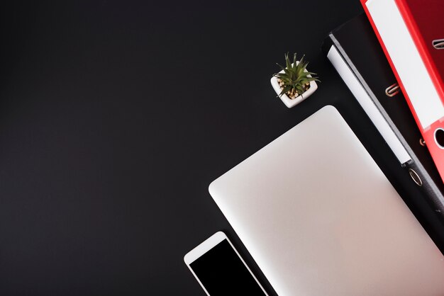 Eine Draufsicht des Mobiltelefons; Laptop; Kaktus Pflanze und Dateien auf schwarzem Hintergrund
