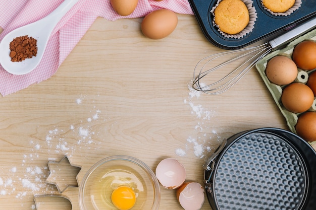 Eine Draufsicht des selbst gemachten kleinen Kuchens und der Bestandteile auf hölzernem Schreibtisch