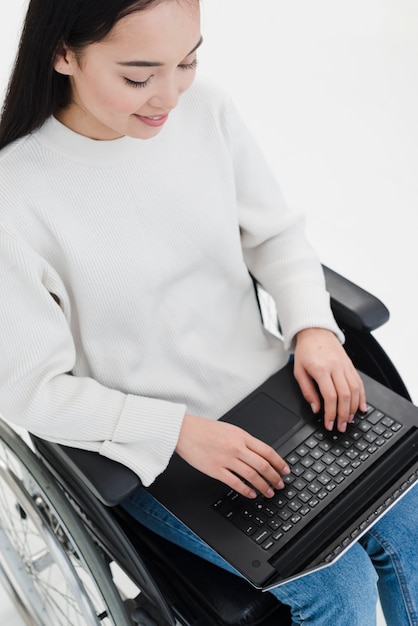 Eine Draufsicht einer jungen Frau, die auf Rollstuhl unter Verwendung des Laptops sitzt